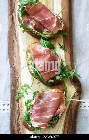 Bruschetta tradizionale italiana con antipasto di pane tostato con formaggio fresco, rucola e prosciutto. Foto Stock