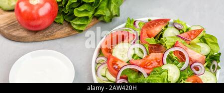 Sano piatto vegetariano a tavola, insalata di verdure con pomodoro fresco, cetriolo, lattuga, cipolla rossa su fondo grigio in cemento. Menù dietetico. Mockup Foto Stock