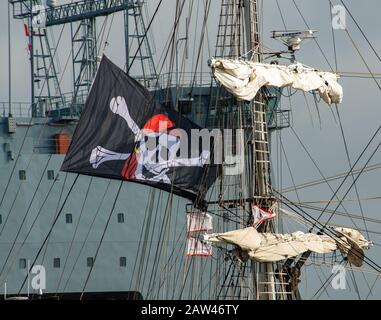 Jolly Roger teschio e croce ossa bandiera volare nella brezza rigida dal rigging della nave alta Mercedes con sfondo grigio nave da guerra. Foto Stock