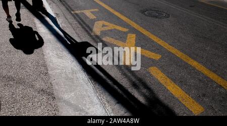 Un cartello di taxi dipinto in giallo sulla strada che segna un taxi rango con ombre dal passatore cadendo attraverso la strada sull'isola greca di Zante. Foto Stock