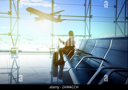 donna che guarda fuori dalla grande finestra all'aeroporto. Stanno prendendo il piacere in aeroplani che si muovono lungo la pista Foto Stock