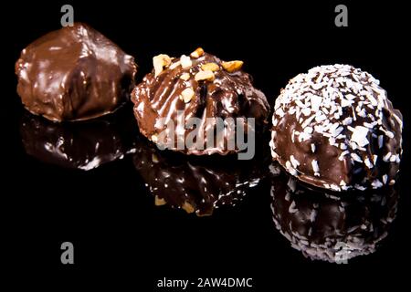 Tre torte di cioccolato su una superficie di specchio nero cosparsa di patatine di cocco e nocciola su uno sfondo scuro Foto Stock