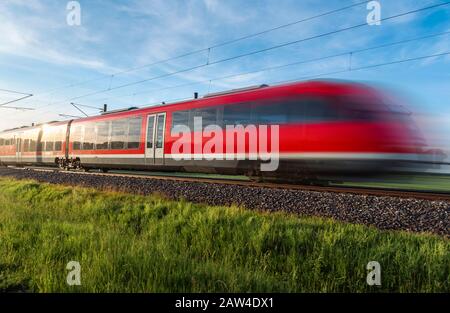 Moderno treno rosso, in movimento blur, viaggiando attraverso la natura verde, la campagna tedesca, in estate giornata di sole, Schwabisch Hall, Germania. Trasporto in treno. Foto Stock