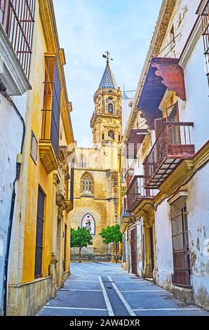 La stretta strada di San Miguel con vecchie case di scaby apre la vista sul campanile panoramico in pietra della Chiesa di San Miguel, Jerez, Spagna Foto Stock