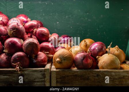 Cipolle rosse e gialle accatastate in scatole di legno inclinate verso il basso con sfondo verde, stanza in alto per scrivere Foto Stock