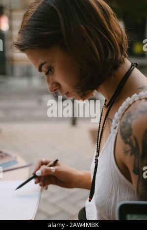 Giovane donna disegna allo sketchbook con una matita all'aperto sulla strada Foto Stock