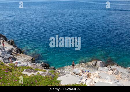 Stoney spiaggia di Hydra Island in Grecia , con bagnanti. Costa del Mar Egeo in una giornata di sole in primavera. Foto Stock