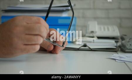 Uomo d'affari Seduto sulla scrivania nel suo ufficio e Tenendo Gli Occhiali in Mano Foto Stock