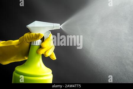 Donna che indossa guanti di gomma gialla con flacone spray verde e spruzzi di nebbia liquida in aria, effetto luce fredda. Molto spazio di copia. Foto Stock
