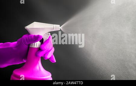 Donna che indossa guanti di gomma rosa con flacone spray rosa e spruzzo di nebbia liquida in aria, effetto luce fredda. Molto spazio di copia. Foto Stock