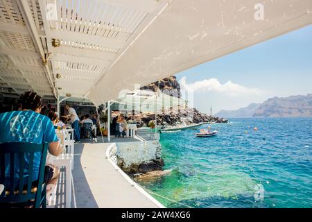 Oia, Santorini/ Grecia 14JUL2019-Ammoudy Bay con barche da pesca e taverne di pesce. I turisti trascorrono del tempo e mangiano nella tradizionale taverna greca. Foto Stock