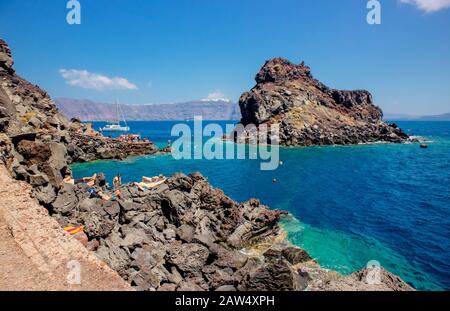 Oia, Santorini / Grecia 14JUL2019-spiaggia Vulcanica di Ammoudy Bay. Sisterhood del viaggio pantaloni location riprese. Persone turisti nuoto e alba Foto Stock