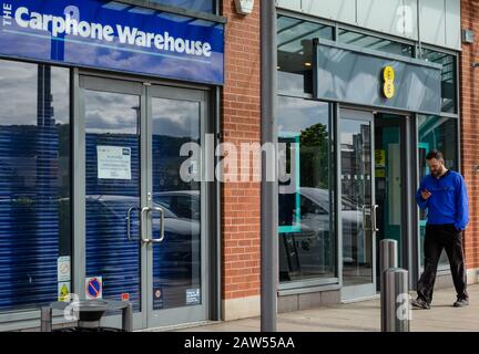 Llanddudno, Regno Unito: 06 maggio 2019: Un uomo controlla il suo telefono cellulare mentre cammina oltre un negozio di telefonia mobile EE aperto. Accanto c'è un ramo del Carphone W. Foto Stock