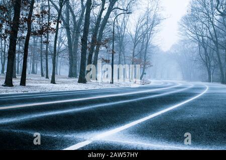 Strada circondata da alberi come neve cade in nevosa inverno giorno. Foto Stock