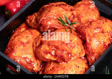 Cosce di pollo. Pollo crudo trapuntato in rosso, marinata di pomodoro su un piatto nero e spezies.Raw carne nella marinata. Foto Stock