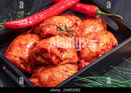 Pollo crudo trapuntato in rosso, marinata di pomodoro su un piatto nero e spezies.Raw carne nella marinata. Foto Stock