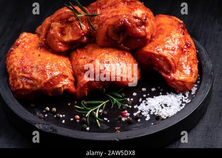 Pollo crudo trapuntato in rosso, marinata di pomodoro su un piatto nero e spezies.Raw carne nella marinata. Foto Stock