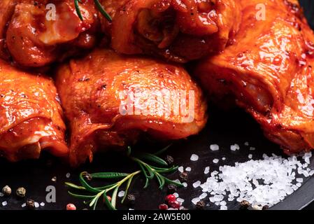 Pollo crudo trapuntato in rosso, marinata di pomodoro su un piatto nero e spezies.Raw carne nella marinata.Dietetica carne. Foto Stock