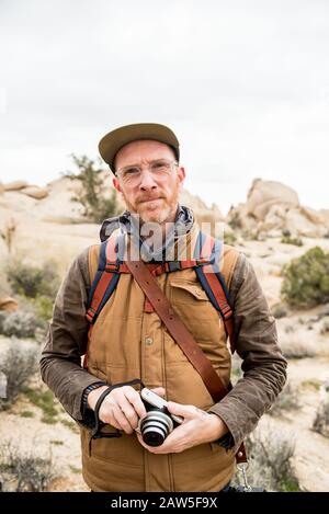 Uomo maturo concentrato con fotocamera e zaino nel deserto Foto Stock