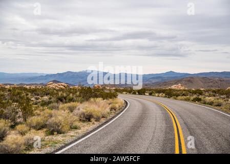 Strada curva nel parco nazionale Joshua Tree che conduce al paesaggio collinare lontano Foto Stock