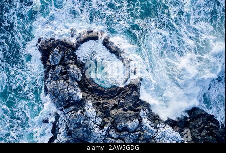 Vista dei drone delle onde che si infrangono sulla scogliera formando schiuma e tuffarsi in mare Foto Stock