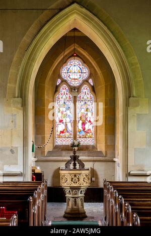 Vetrate colorate, font battesimale e architettura gotica della chiesa di San Barnaba a Snowshill, Gloucestershire, Inghilterra, Regno Unito Foto Stock