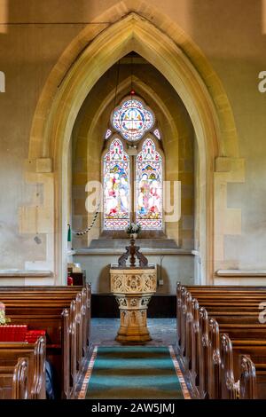 Vetrate colorate, font battesimale e architettura gotica della chiesa di San Barnaba a Snowshill, Gloucestershire, Inghilterra, Regno Unito Foto Stock