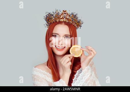 Bellezza regina e vitamina C. una giovane donna che tiene fetta di arancio sorridente bella donna con cristallo corona sulla testa isolato su sfondo grigio chiaro wa Foto Stock