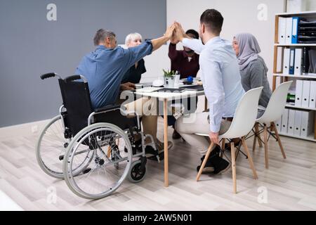 Un Uomo D'Affari Disabile Che Dà Cinque Anni Di Altezza Ai Suoi Partner Sorridenti In Ufficio Foto Stock