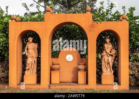 Waimea, Hawaii, Stati Uniti. - 15 Gennaio 2020: Sede Centrale Di Parker Ranch. Statua arancione in giardino che mostra tre archi sotto cui due donne e pentole. Verde fo Foto Stock