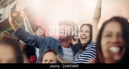 Coppia entusiasta che si rallegrano e prende selfie mentre si trova allo stadio. Allegri tifosi di calcio che prendono selfie mentre si guarda la partita nello stadio. Foto Stock