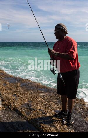 Un pescatore di Treasure Coast sul molo al Fort Pierce inlet controlla la sua linea dopo aver rimosso un pesce nella contea di St. Lucie, Florida, USA . Foto Stock