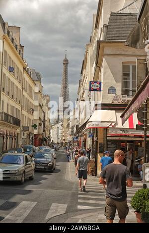 Una classica vista parigina della Torre Eiffel con persone che camminano in Rue Saint-Dominique, automobili, finestre, caffetterie e negozi, fiancheggiano il canyon della strada stretta Foto Stock