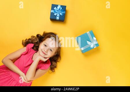 Affascinante ragazza sognante circondata da scatole con regali. Vista dall'alto su un simpatico bambino su uno sfondo giallo. Foto Stock