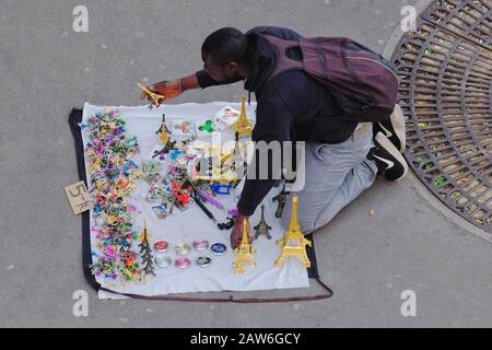 Un venditore di strada illegale che vende souvenir multicolori della Torre Eiffel a Parigi inginocchiati su un panno aperto che si trasforma in una borsa per il trasporto Foto Stock