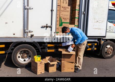 Un delirante che indossa una maschera facciale durante un focolaio di coronavirus scarica un camion che trasporta vari articoli da tavola e da sole a Kampong Cham, Cambogia. Foto Stock