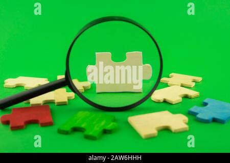 Pezzi di puzzle colorati con lente di ingrandimento focalizzata su un singolo pezzo d'angolo bianco in un'immagine concettuale sul verde per la ricerca, l'indagine Foto Stock