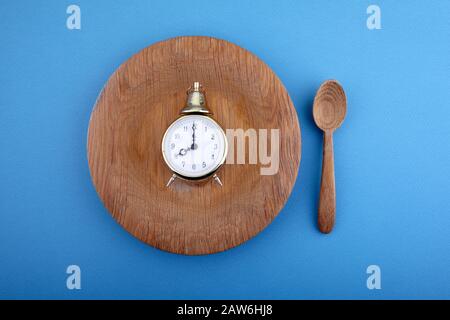 Concetto di finestra di alimentazione di otto ore o orario di colazione con orologio sul piatto e cucchiaio di legno. Vista dall'alto Foto Stock
