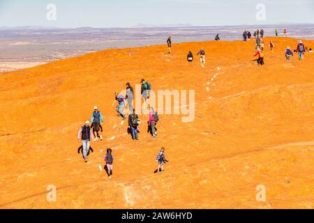 Una linea di turisti fa l'ultimo trekking lungo la cima di Uluru nell'ultimo mese prima che sia chiuso agli arrampicatori. Foto Stock