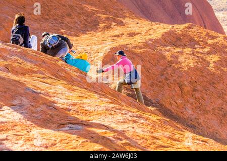 I turisti si arrampicano sul ripido terreno ondulato sulla cima di Uluru. Northern Territory, Australia Foto Stock