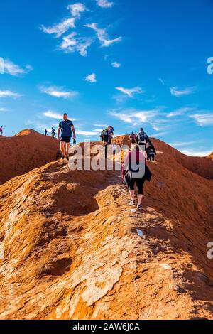 I turisti si arrampicano sul ripido terreno ondulato sulla cima di Uluru. Northern Territory, Australia Foto Stock