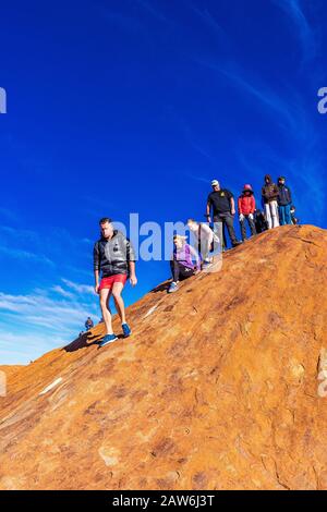 I turisti si arrampicano sul ripido terreno ondulato sulla cima di Uluru. Northern Territory, Australia Foto Stock