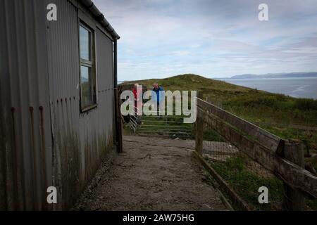 GP Dr David Binnie chattando per paziente Walter Williams a casa sua a Kiloran Bay sulla Interna isola Hebridean di Colonsay sulla costa occidentale della Scozia. L'isola si trova nella zona del consiglio di Argyll e Bute e ha una superficie di 4.074 ettari (15,7 mi quadrati). Allineato sull'asse sud-ovest a nord-est, misura 13 km di lunghezza e raggiunge 4,8 km al suo punto più ampio, nel 2019 ha una popolazione permanente di 136 adulti e bambini. Foto Stock