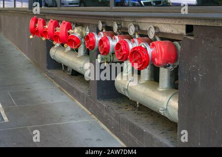 Idranti luminosi in fila con tubi in metallo e tappi rossi. Infrastrutture urbane industriali Foto Stock