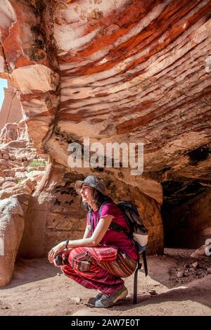 Donna viaggiatore che riposa all'entrata di una tomba abbandonata a Petra, Giordania Foto Stock