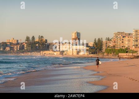 Sydney, Australia - 14 aprile 2017: Surfista in una muta con surf board a piedi in spiaggia Foto Stock