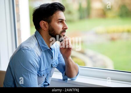 Uomo che guarda fuori della finestra Foto Stock