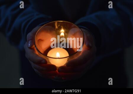 mani di bambino intorno ad una candela bruciante nel buio Foto Stock