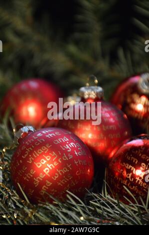 Palline di Natale rosse su buughs sempreverdi con la storia di presepe scritta su di loro Foto Stock