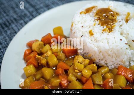 Riso cotto, curry con pollo, carota e patate da vicino su un piatto su un tavolo. Foto Stock